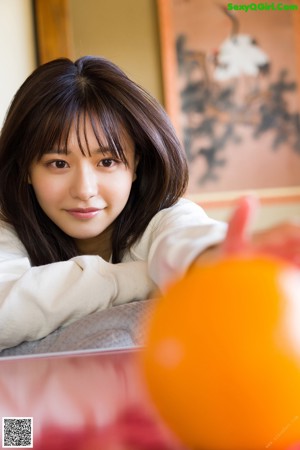 A woman sitting at a table with an orange in front of her.