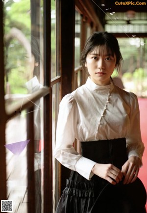 A woman in a white shirt leaning against a window.