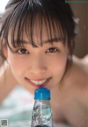 A naked asian woman sitting at a table with a bottle of water.