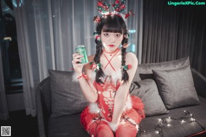 A woman in a red dress sitting on a couch drinking from a can.