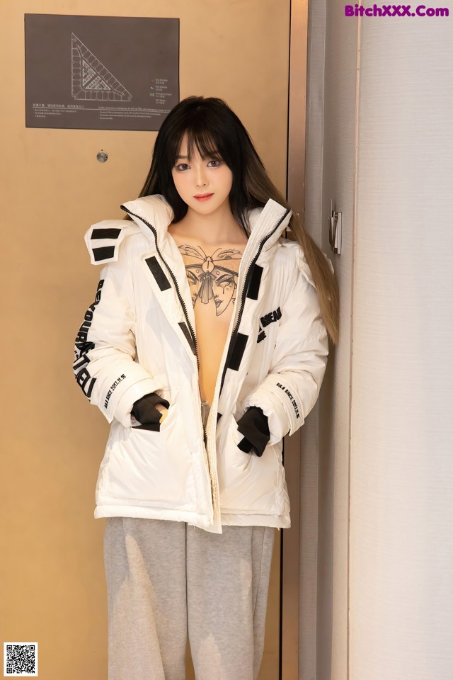 A woman standing in front of a door wearing a white jacket.