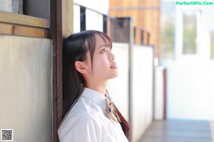 A young woman in a school uniform sitting on a wooden floor.