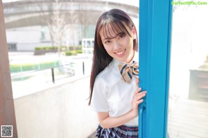 A young woman in a school uniform leaning against a blue door.