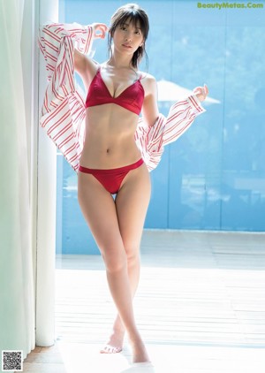 A woman in a pink bodysuit leaning against a wall.