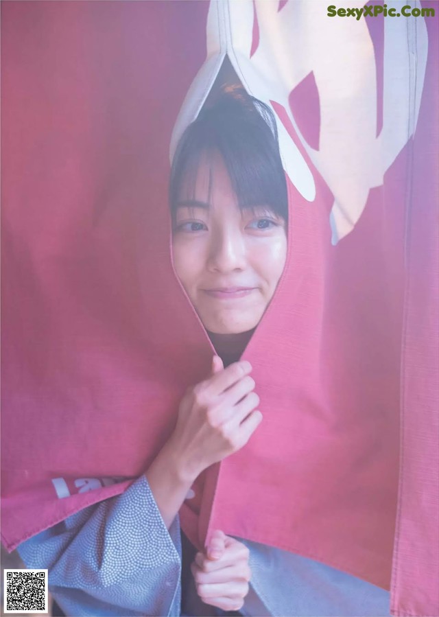 A woman in a kimono is peeking out from behind a pink curtain.