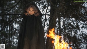 A woman sitting in front of a fire in the woods.