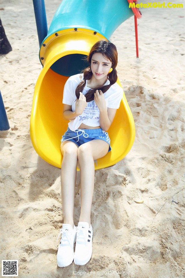 A woman sitting on a yellow slide in the sand.