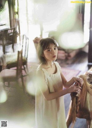 A woman in a white dress standing next to a rocking horse.