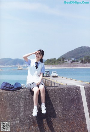 A woman sitting on a concrete wall by the water.